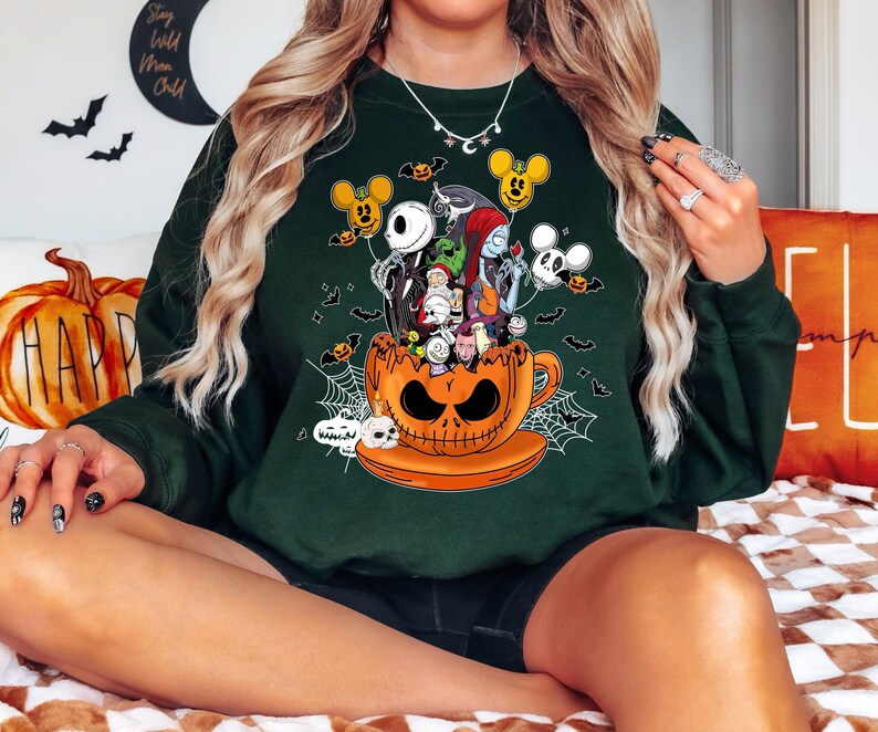 Op de afbeelding: Donkergroene sweatshirt met een Halloween-thema. Het ontwerp bevat personages uit The Nightmare Before Christmas, een pompoen theekopje, vleermuizen en Mickey Mouse-vormige ballonnen. Een comfortabele, casual stijl.