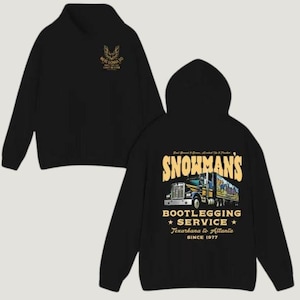 May include: Black hoodie with a high collar and a hood. The front features a gold emblem and text. The back displays a graphic of a semi-truck with the words "SNOWMAN'S BOOTLEGGING SERVICE" and "Texarkana to Atlanta SINCE 1977".