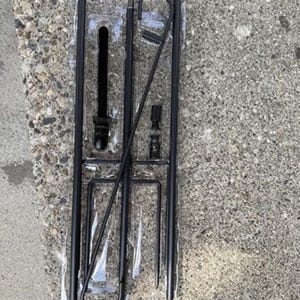 May include: A set of black metal garden stakes and supports, packaged in clear plastic. The stakes have pointed ends for ground insertion and various attachments for plant support. The items are arranged on a textured gray surface.