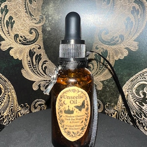 Puede incluir: Una botella de vidrio marrón con un cuentagotas negro y un dije plateado. La botella tiene una etiqueta con el texto "Unseelie Oil" y otro texto. Una cinta negra está unida a la botella. El fondo es un patrón ornamental verde oscuro y dorado.
