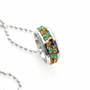 May include: A silver chain necklace with a silver ring pendant. The ring is decorated with a band of colorful gemstones.