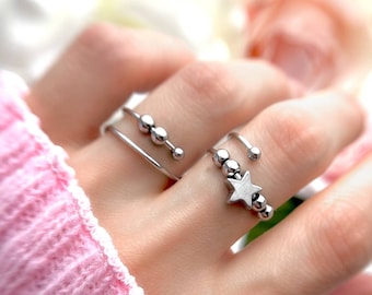 May include: A silver ring featuring a star charm and a row of small beads. The ring is worn on a finger with a simple silver band.