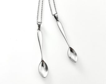 May include: Two silver spoon necklaces with delicate chains. The spoons are a simple design with a rounded bowl and a long handle.