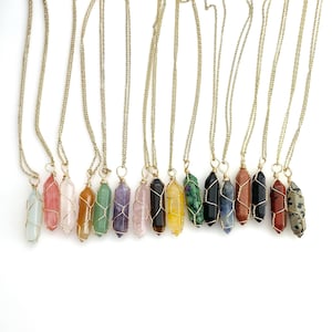 May include: A set of 12 gold chain necklaces with different colored crystal point pendants. The pendants are wrapped in gold wire and include amethyst, rose quartz, green aventurine, clear quartz, tiger's eye, citrine, green aventurine, sodalite, red jasper, and dalmatian jasper.