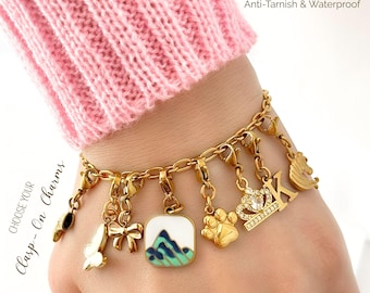 Op de afbeelding: Een 18k goudkleurige roestvrijstalen schakelarmband met diverse afneembare bedels met karabijnsluiting, waaronder een vlinder, strik, berglandschap, pootafdruk, kroon, letter K en paardenkop. Tekst: 18k Gold Stainless Steel Anti-Tarnish & Waterproof.