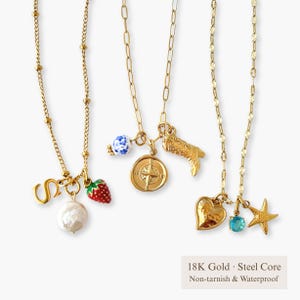 以下が含まれることがあります： ゴールドトーンのネックレス。チャームは「S」の文字、イチゴ、パール、コンパス、カウボーイブーツ、ハート、青い宝石、ヒトデ。白い背景。テキスト「18K Gold • Steel Core Non-tarnish & Waterproof」が表示されています。