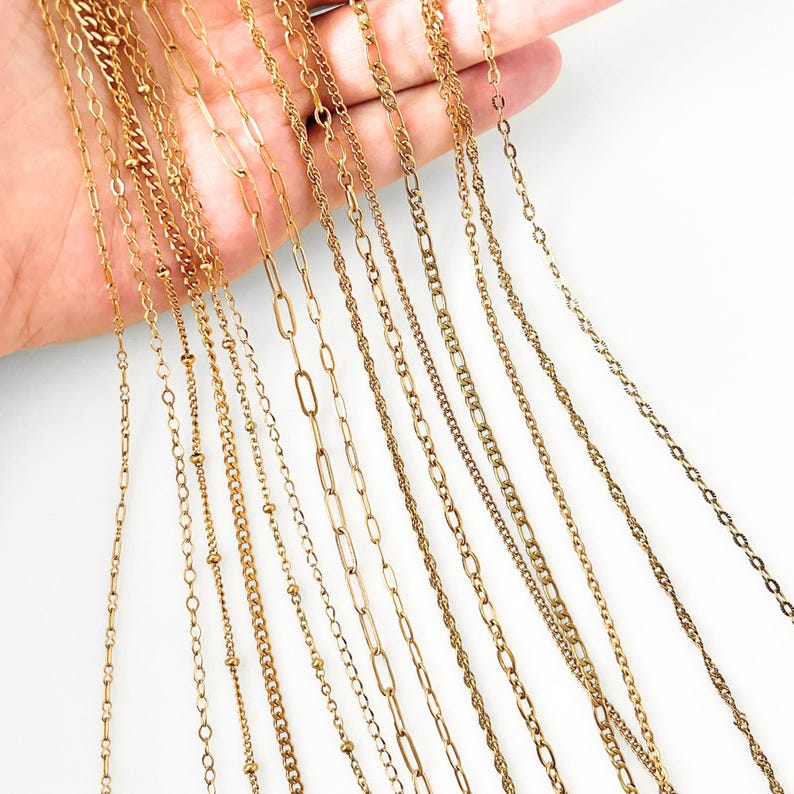 May include: A collection of ten distinct gold-toned metal chains displayed in a row. The assortment includes various link styles such as cable, paperclip, rope, ball, and figaro chains, all featuring a polished metallic finish and uniform color.