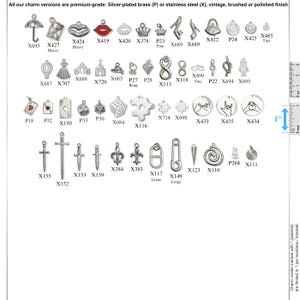 May include: A collection of silver-toned metal charms in various shapes including umbrellas, crowns, swords, and symbols, labeled with alphanumeric codes. A vertical ruler on the right side indicates a 1-inch scale for size reference.