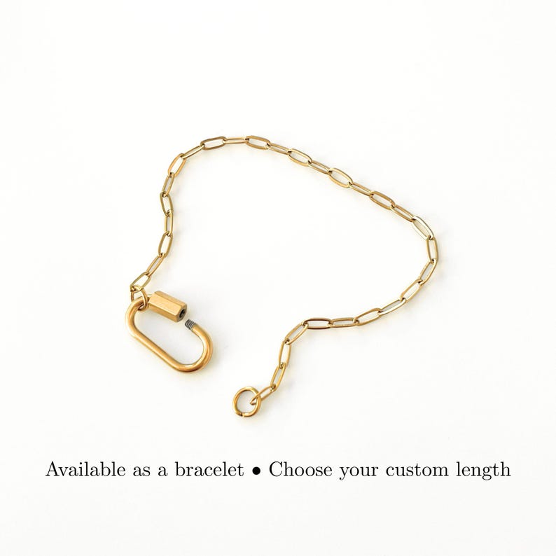 May include: A gold-toned chain bracelet featuring elongated oval links and a large, functional carabiner-style clasp. The text below the jewelry reads: Available as a bracelet &bull; Choose your custom length. The design is simple and metallic.