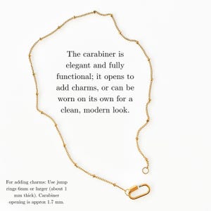 May include: A gold-toned chain necklace featuring small evenly spaced beads and a functional carabiner clasp. The text reads: The carabiner is elegant and fully functional; it opens to add charms, or can be worn on its own for a clean, modern look. For adding charms: Use jump rings 6mm or larger (about 1 mm thick). Carabiner opening is approx 1.7 mm.