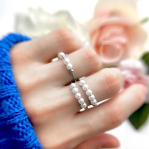 May include: Two pearl rings on a hand. The rings are made of small white pearls and a silver chain.