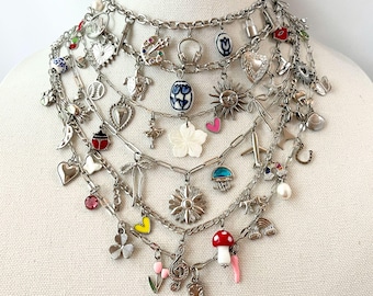 May include: A multi-layered silver-tone chain necklace featuring an extensive collection of assorted charms, including a sun, a mushroom, a treble clef, a cowboy boot, a flower, a turtle, a heart, a ladybug, a plane, and various colorful beads.