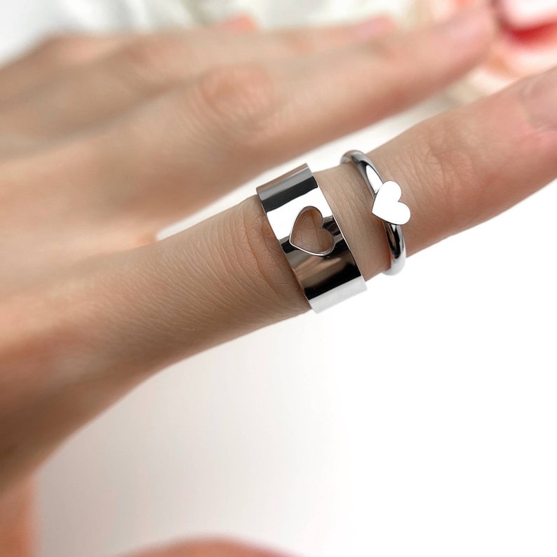 Op de afbeelding: Twee zilveren ringen met hartvormige uitsparingen. De ring aan de linkerkant heeft een grotere hartvormige uitsparing en de ring aan de rechterkant heeft een kleinere hartvormige uitsparing.