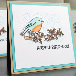 blue bird sitting on a branch with happy bird day stamped underneath