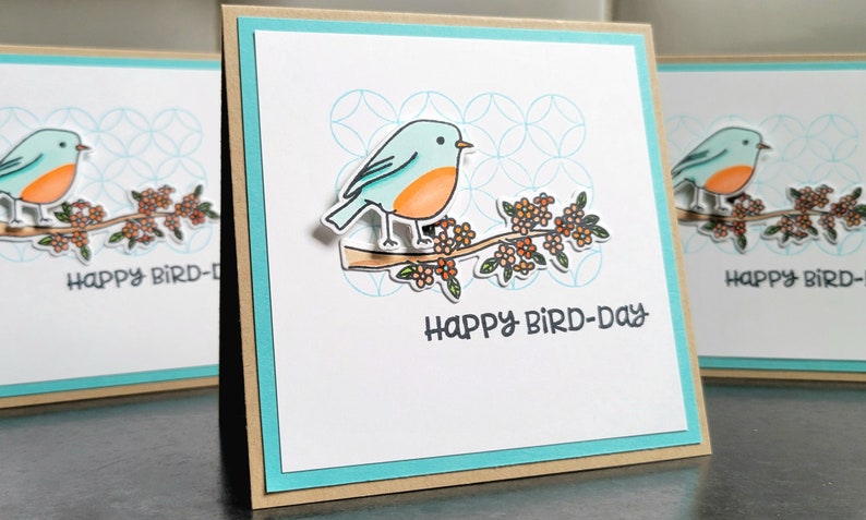 blue bird sitting on a branch with happy bird day stamped underneath