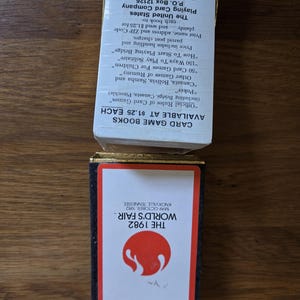 May include: A vintage card game box from the 1982 World's Fair in Knoxville, Tennessee. The box features a red and white design with the fair's logo. The text on the box includes the fair's name and dates.