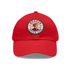 Könnte beinhalten: Eine leuchtend rote Baseballkappe mit einem kreisförmigen Aufnäher. Der Aufnäher zeigt den Text "QUAKER SPICE LIFE" und eine Illustration einer Frau mit Haube. Die Kappe hat einen gebogenen Schirm und einen verstellbaren Riemen.