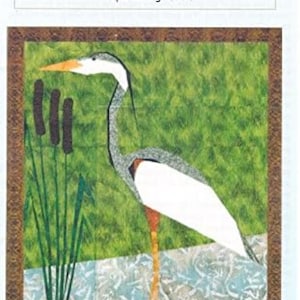 May include: A paper piecing pattern titled "039 Great Blue Heron." The artwork depicts a heron with white, gray, and orange plumage, standing in water. The image is 16" x 24" without borders, with a green and brown background.