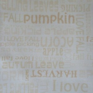 May include: Off-white fabric with a repeating pattern of fall-themed words in a light brown color. Words include "pumpkin," "autumn," "harvest," and "apple picking."