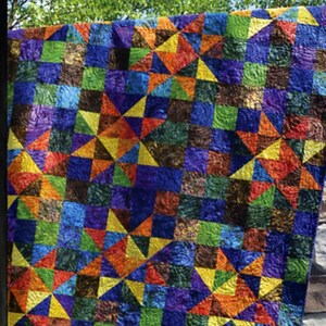May include: A colorful quilt with a starburst design, featuring squares and triangles in shades of blue, green, orange, yellow, and purple. The quilt is hanging outdoors. The word "Twinkle" is at the top, and the "Swirly Girls" logo is at the bottom.