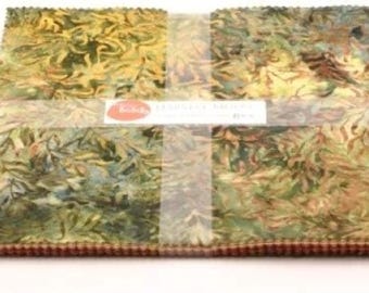May include: A stack of fabric squares with a leaf pattern in shades of green, yellow, and brown. The fabric is bound with a clear band and a label with text. The edges of the fabric are a dark brown color.