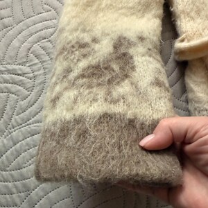 May include: Close-up of a beige and brown knitted sleeve. The sleeve has a textured, fuzzy appearance with a patterned design in the middle. The cuff is a darker shade of brown.