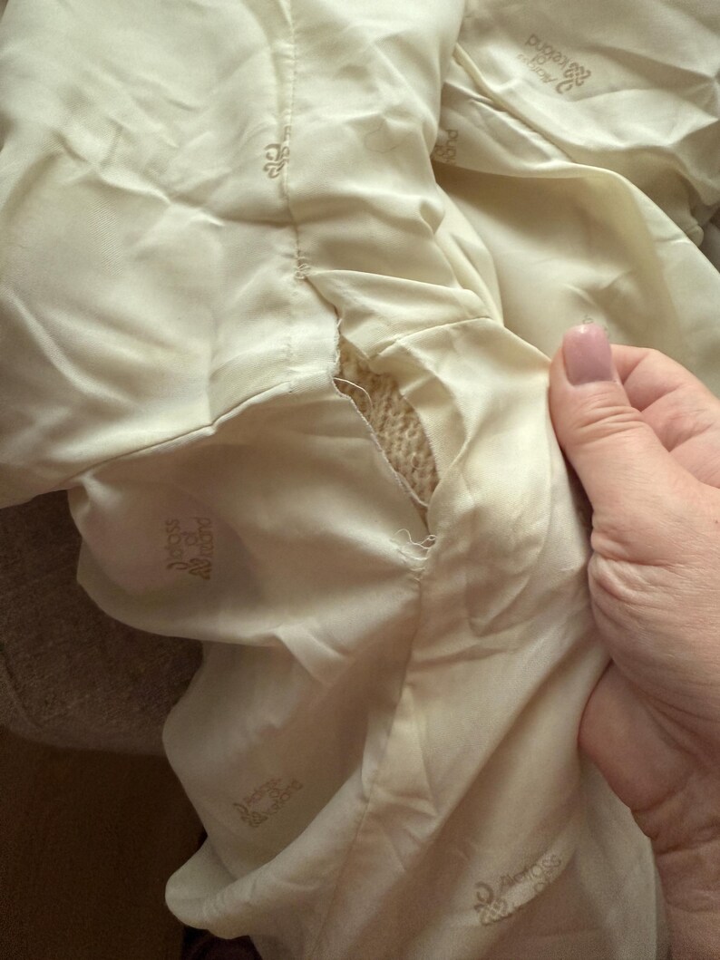 May include: Close-up of a cream-colored fabric with a tear revealing a woven texture underneath. The fabric has a sheen and appears to be part of a garment. The words "Deluxe Allround" are printed on the fabric.
