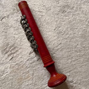 May include: A red wooden musical instrument with silver metal accents. The instrument has a cylindrical body with decorative yellow stripes and a flared base. The silver accents are linked together in a chain-like pattern.