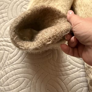 May include: Close-up of a beige and brown sleeve cuff. The cuff is made of a soft, fuzzy material. The interior of the cuff is a lighter beige color. The sleeve appears to be part of a sweater or coat.