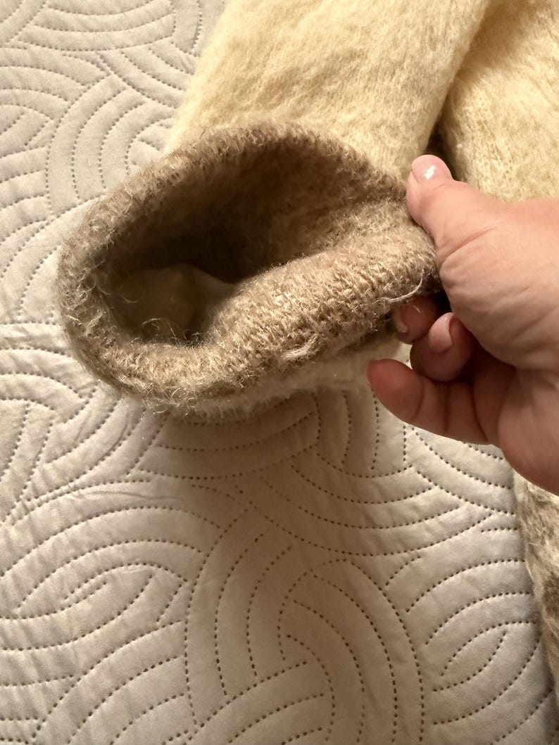 May include: Close-up of a beige and brown sleeve cuff. The cuff is made of a soft, fuzzy material. The interior of the cuff is a lighter beige color. The sleeve appears to be part of a sweater or coat.
