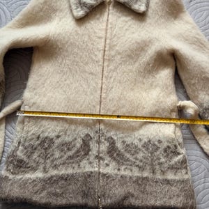May include: Cream-colored zip-up coat with a faux fur collar and trim. The coat features a decorative pattern in shades of gray near the hem. Includes a matching belt. The coat measures approximately 30 inches in length.
