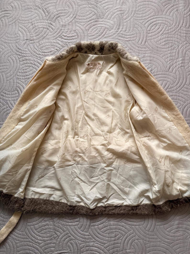 May include: Cream-colored vintage jacket with a brown fur trim around the collar and hem. The interior lining is a light cream color. The jacket has a matching belt and a label inside.
