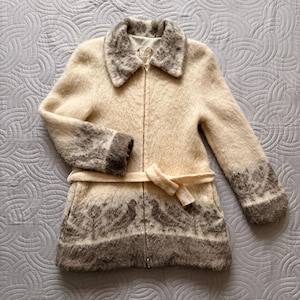 May include: A cream-colored wool coat with a zip-up front, a collar, and a matching belt. The coat features brown patterned accents on the collar, cuffs, and hem. The coat is a mid-length style.