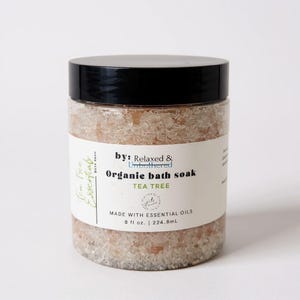 May include: A clear plastic jar with a black lid filled with pinkish bath soak crystals. The label reads "Organic bath soak TEA TREE" and "MADE WITH ESSENTIAL OILS". The jar contains 8 fl oz.