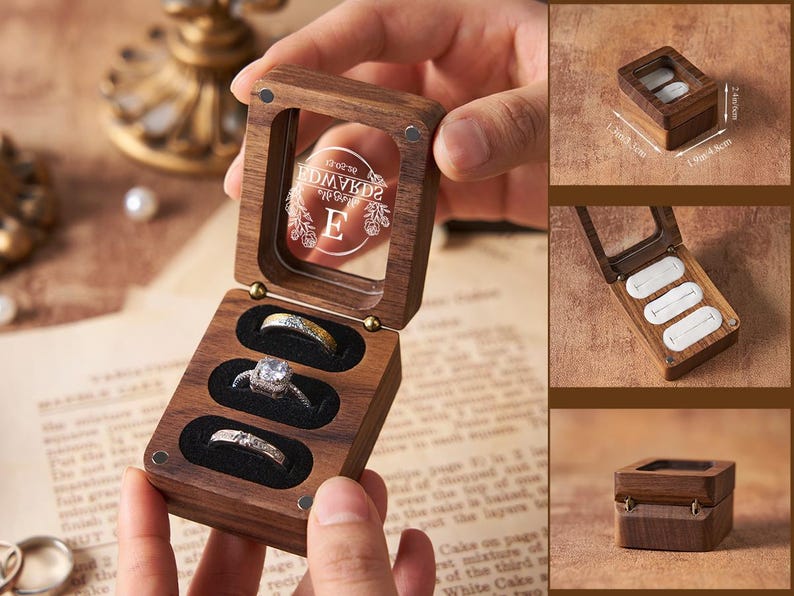 May include: A wooden ring box with a clear lid, holding three rings. The box is open, revealing the rings in black velvet slots. The lid has etched text and a decorative design. The box is 1.9 inches long, 1.9 inches wide, and 0.9 inches high.