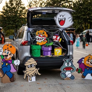 Może przedstawiać: Dekoracja bagażnika samochodu z motywem Halloween i Super Mario. Wycinanki przedstawiają Mario w masce dyni, mumię, zombie Goombę, Mario wampira, ducha Boo, roślinę Piranha w dyni oraz żółty blok z pytajnikiem.