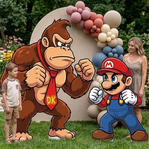 May include: Large cardboard cutouts of Donkey Kong and Mario standing on a green lawn. Donkey Kong is brown with a red tie featuring the letters DK. Mario wears a red hat with an M, a blue jumpsuit, and white gloves. A balloon arch is behind them.