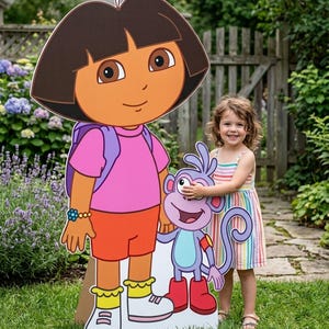 Puede incluir: Un expositor de cartón grande, plano y troquelado que muestra al personaje de dibujos animados Dora con su mochila morada, pantalones cortos naranjas y camiseta rosa, junto a su compañero mono Botas, de color morado y botas rojas.