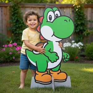 Puede incluir: Un gran recorte de Yoshi verde de la serie de videojuegos Super Mario. El recorte tiene una panza blanca, detalles rojos y zapatos naranjas. Un niño sostiene el recorte en un jardín cubierto de hierba.