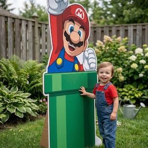 May include: A large, flat, cardboard cutout of the video game character Mario, depicted with a red hat featuring a white M, blue overalls, and a red shirt, emerging from a tall, green, cylindrical pipe with a wide rim and a vertical striped pattern.