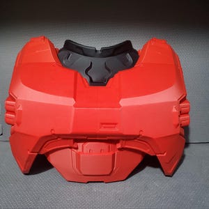 Könnte beinhalten: Ein rotes Brustpanzerteil aus Kunststoff mit einem schwarzen Nackenschutz. Die Rüstung hat ein futuristisches Design mit mehreren Paneelen und Rippen. Das Teil ist wahrscheinlich Teil eines Kostüms oder Cosplays.