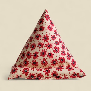 Könnte beinhalten: Ein dreieckiges Buchkissen mit einem Muster aus roten Blumen mit schwarzen Zentren auf cremefarbenem Hintergrund. Das Kissen dient zur Unterstützung von Büchern oder Tablets, ca. 30 cm hoch.