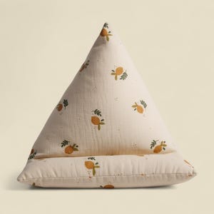 Pode incluir: Uma almofada triangular creme com um padrão de limões. A almofada tem um aspeto macio e texturizado e apresenta ilustrações repetidas de limões amarelos com folhas verdes. O design é simples e adequado para um quarto infantil.