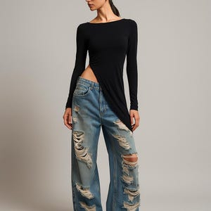 Puede incluir: Top negro de manga larga con diseño asimétrico y cuello barco. El top se combina con vaqueros anchos, desgastados y de color azul claro. Los vaqueros tienen múltiples roturas y desgarros en las piernas, creando un look casual y atrevido.