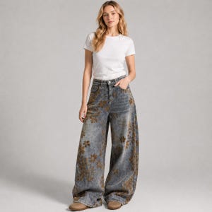 Op de afbeelding: Een vrouw draagt een wit t-shirt en een jeans met wijde pijpen. De jeans is verbleekt blauw met een bruin bloemenpatroon. De jeans heeft een hoge taille en een relaxte pasvorm.