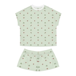May include: A light green pajama set with a repeating pattern of small green frogs and red mushrooms. The set comprises a short-sleeved top with a white collar and matching shorts. The fabric looks soft and comfortable.