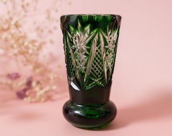 May include: A dark green cut glass vase featuring a flared rim and a rounded base. The upper portion of the vase is decorated with intricate geometric patterns, including star-like motifs and a cross-hatched diamond design cut into the glass.