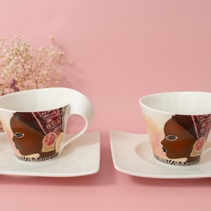 May include: A white ceramic mug with a black handle and the text "But First, Coffee" in a bold, black font. The mug is set against a blurred background, suggesting a cozy setting.