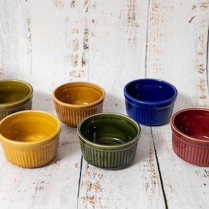 Puede incluir: Conjunto de seis ramequines de cerámica en varios colores: verde oliva, amarillo mostaza, azul marino y rojo oscuro. Cada ramequín tiene un exterior acanalado y un interior liso, ideal para hornear y servir porciones individuales.