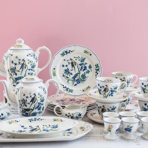 Könnte beinhalten: Ein komplettes Tee- und Essservice aus Porzellan mit Vogel- und Blumenmuster. Das Set beinhaltet eine Teekanne, eine Zuckerdose, einen Sahnekännchen, Teller, Tassen, Untertassen, Servierplatten und Eierbecher. Das Farbschema ist Weiß, Blau und Gelb.